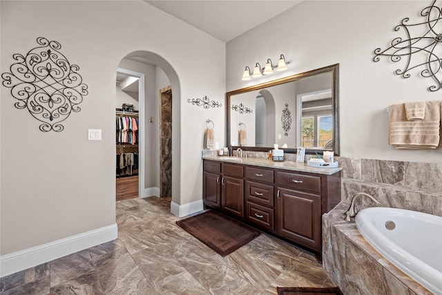 bathroom featuring a walk in closet, baseboards, a bath, and vanity