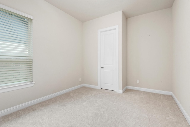 spare room featuring light colored carpet and baseboards