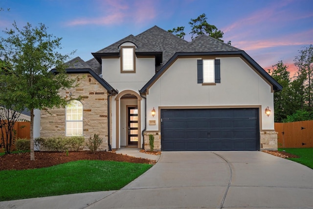 french provincial home with fence, roof with shingles, a garage, stone siding, and driveway