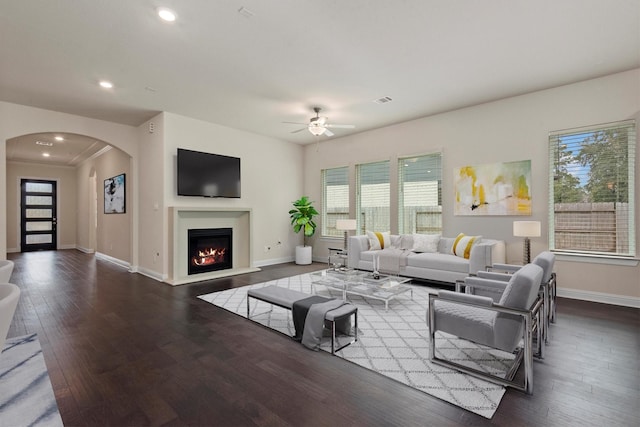 living room featuring wood finished floors, arched walkways, a warm lit fireplace, and baseboards