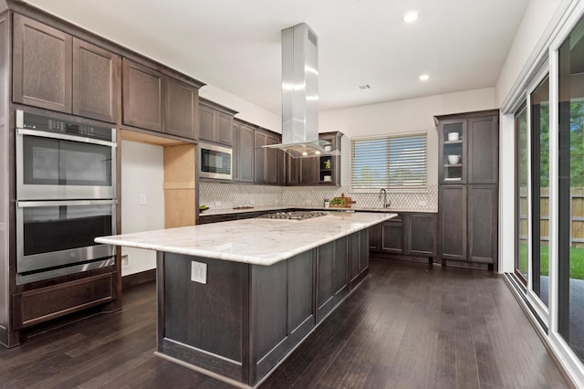 kitchen featuring tasteful backsplash, dark brown cabinets, island range hood, stainless steel appliances, and dark wood-style flooring