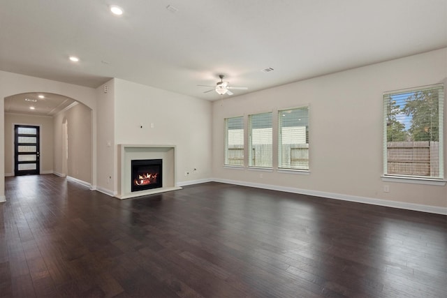 unfurnished living room featuring arched walkways, a warm lit fireplace, baseboards, and dark wood-style flooring