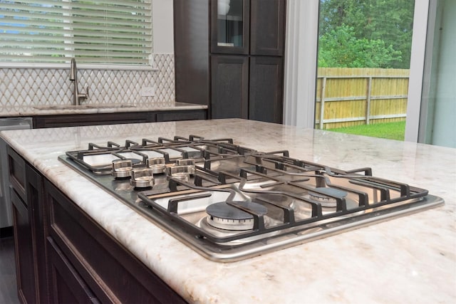 details featuring a sink, light stone counters, backsplash, stainless steel gas stovetop, and dark brown cabinets