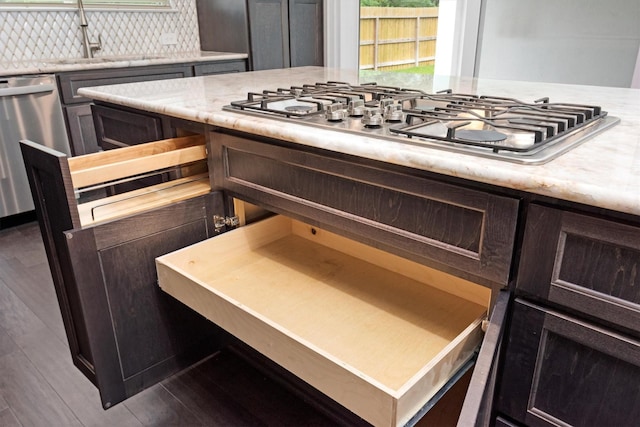 kitchen with wood finished floors, a sink, stainless steel appliances, dark brown cabinets, and backsplash