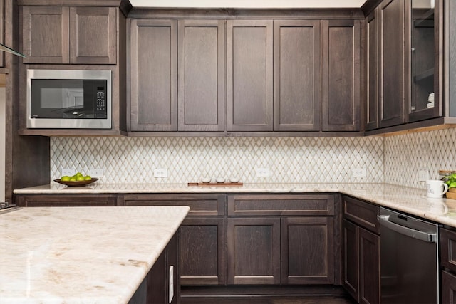 kitchen featuring light stone countertops, stainless steel appliances, decorative backsplash, dark brown cabinetry, and glass insert cabinets