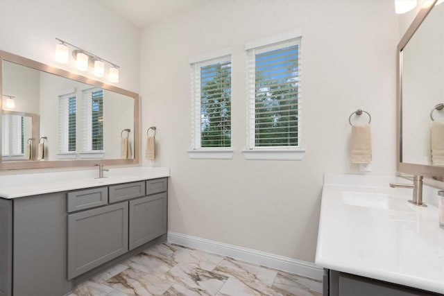 full bath with two vanities, baseboards, marble finish floor, and a sink