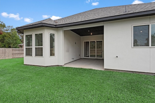 rear view of house featuring a shingled roof, fence, stucco siding, a yard, and a patio area