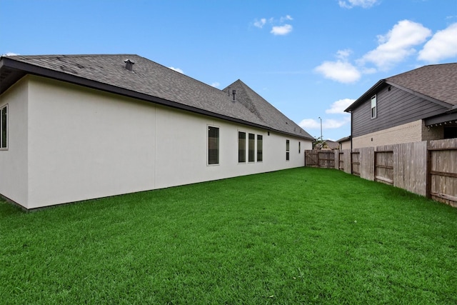 back of house featuring stucco siding, a lawn, a fenced backyard, and a shingled roof