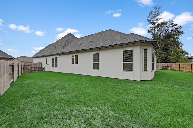 rear view of house featuring central AC, roof with shingles, stucco siding, a lawn, and a fenced backyard