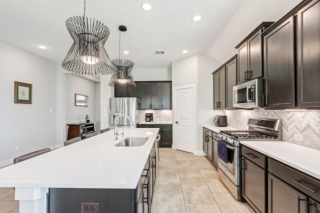 kitchen with a center island with sink, light countertops, hanging light fixtures, stainless steel appliances, and a sink