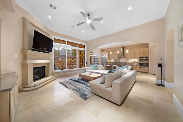 living area featuring arched walkways, a glass covered fireplace, crown molding, and baseboards