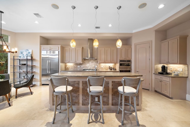 kitchen with visible vents, wall chimney range hood, a center island with sink, ornamental molding, and appliances with stainless steel finishes