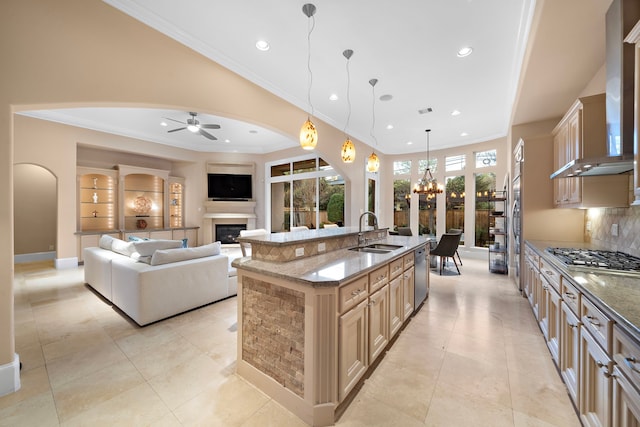 kitchen featuring a sink, open floor plan, a glass covered fireplace, appliances with stainless steel finishes, and wall chimney range hood