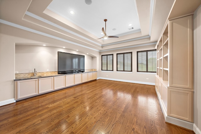 unfurnished living room featuring a sink, a raised ceiling, light wood-style floors, and ornamental molding