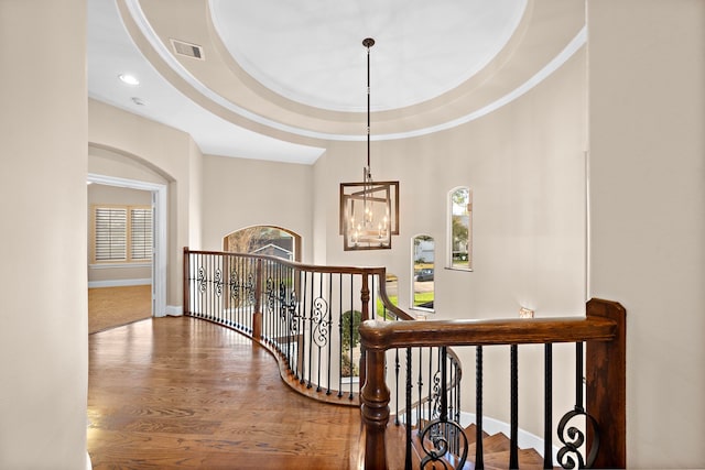 stairs with a notable chandelier, a raised ceiling, ornamental molding, wood finished floors, and baseboards