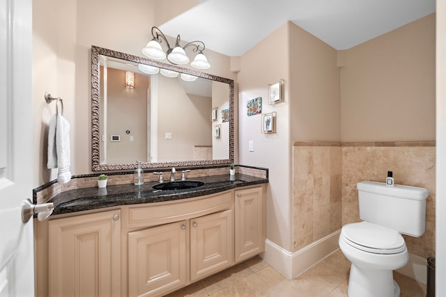 bathroom featuring tile patterned flooring, tile walls, toilet, wainscoting, and vanity