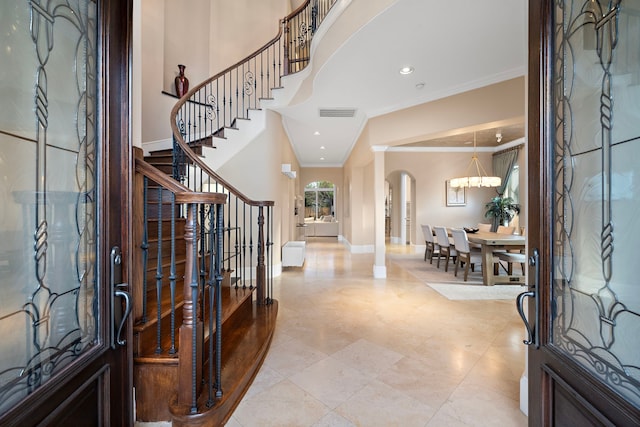 foyer featuring arched walkways, an inviting chandelier, crown molding, baseboards, and stairs