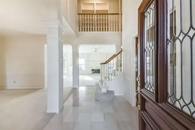 foyer entrance with ceiling fan, stairway, a high ceiling, a decorative wall, and ornate columns