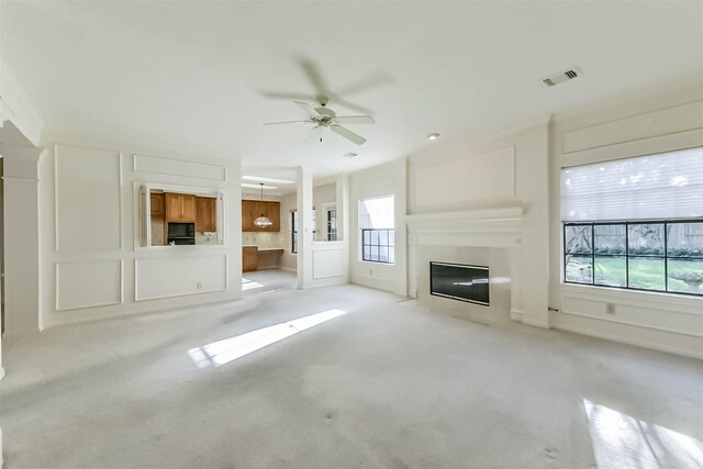 unfurnished living room with visible vents, a fireplace with flush hearth, ceiling fan, light carpet, and a decorative wall