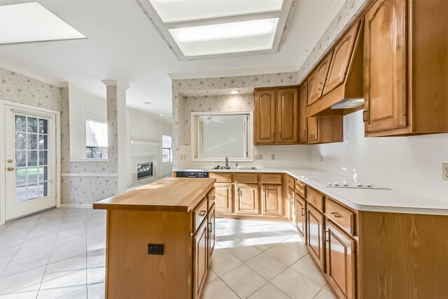 kitchen with wooden counters, wallpapered walls, white electric cooktop, a glass covered fireplace, and a sink