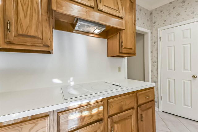 kitchen with wallpapered walls, light tile patterned flooring, light countertops, under cabinet range hood, and white electric cooktop