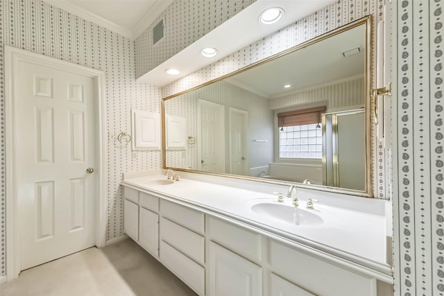 full bathroom with wallpapered walls, crown molding, double vanity, a stall shower, and a sink