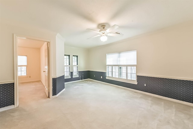 empty room featuring wallpapered walls, carpet flooring, a ceiling fan, and wainscoting