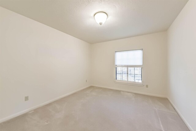 unfurnished room featuring light carpet, a textured ceiling, and baseboards