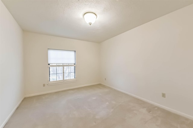 unfurnished room featuring a textured ceiling, baseboards, and light carpet