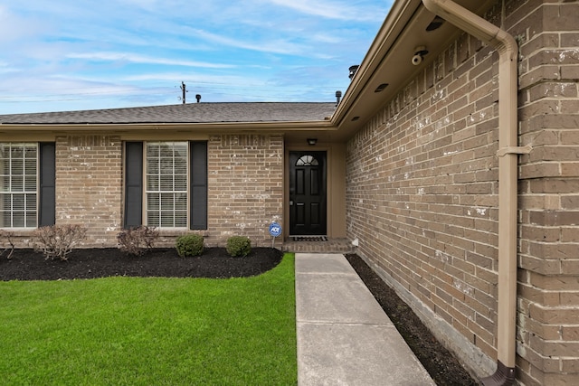 entrance to property featuring brick siding, a lawn, and roof with shingles