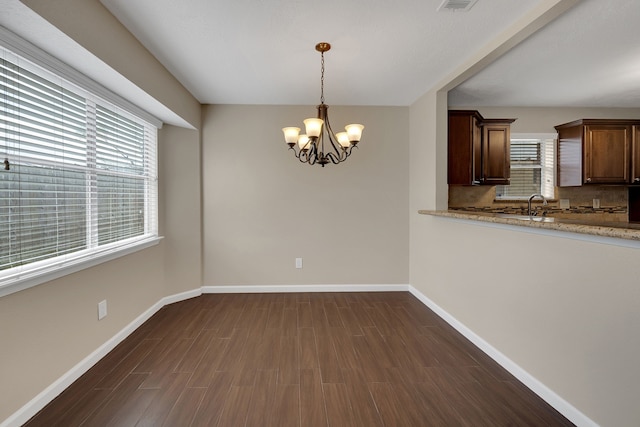 unfurnished dining area featuring dark wood-style floors, visible vents, baseboards, a sink, and a chandelier