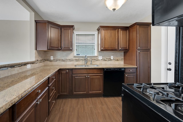 kitchen featuring wood finished floors, light stone countertops, a sink, black appliances, and tasteful backsplash