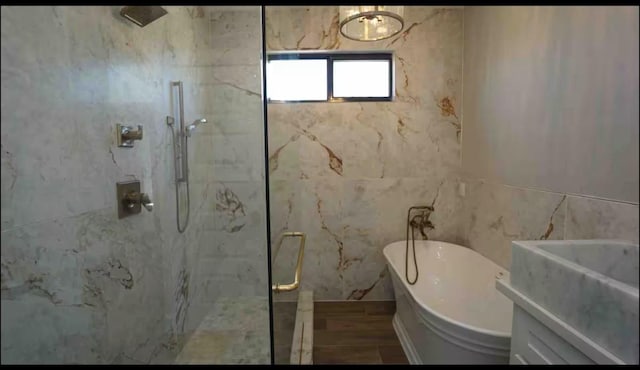 full bath featuring a freestanding tub, wood finished floors, a marble finish shower, tile walls, and vanity