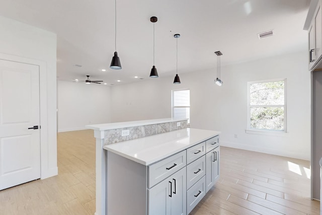 kitchen featuring visible vents, light wood finished floors, a kitchen island, light countertops, and pendant lighting