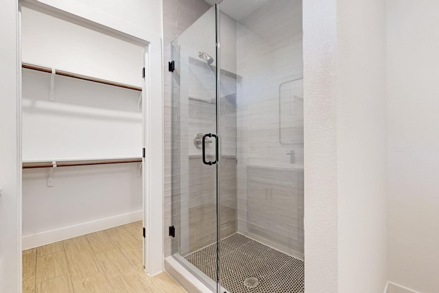 bathroom featuring wood finished floors, a walk in closet, baseboards, and a stall shower