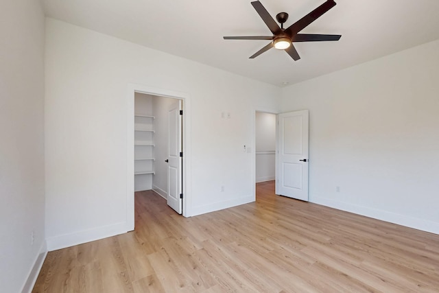 unfurnished bedroom featuring a spacious closet, light wood-style flooring, and baseboards