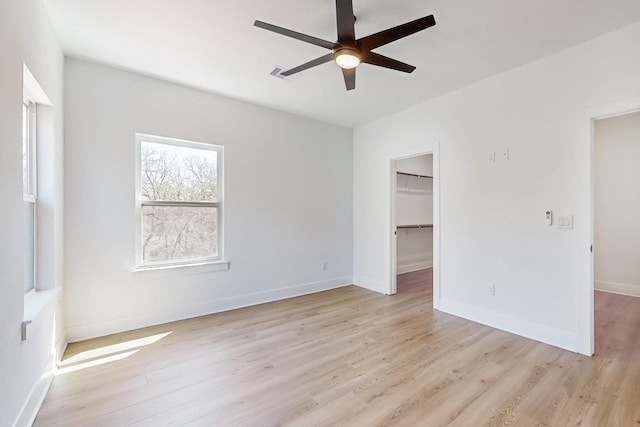 unfurnished bedroom featuring a walk in closet, baseboards, visible vents, and light wood finished floors