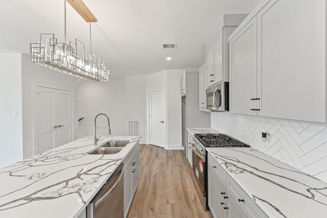 kitchen featuring visible vents, a sink, tasteful backsplash, light wood-style floors, and appliances with stainless steel finishes