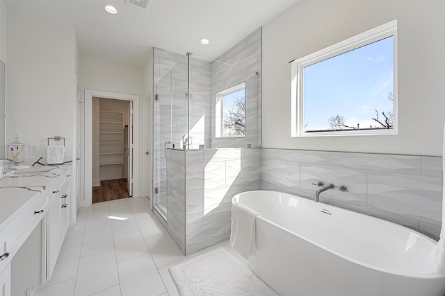 full bath with a shower stall, a walk in closet, a freestanding bath, vanity, and tile walls