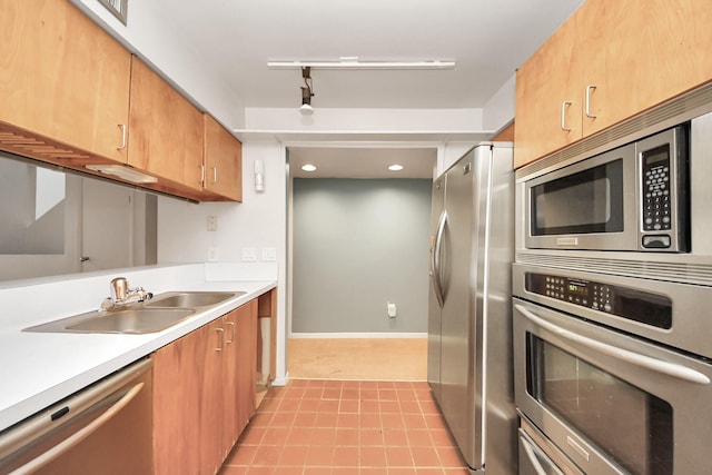 kitchen featuring track lighting, a sink, appliances with stainless steel finishes, light countertops, and baseboards