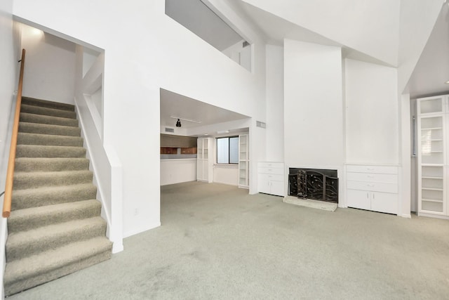 unfurnished living room with visible vents, a fireplace with raised hearth, stairs, carpet flooring, and a high ceiling