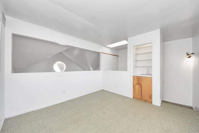 interior space featuring built in shelves, baseboards, a sink, vaulted ceiling, and light carpet