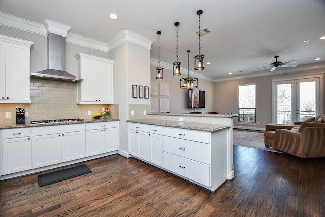 kitchen featuring visible vents, open floor plan, a peninsula, wall chimney range hood, and stainless steel gas cooktop