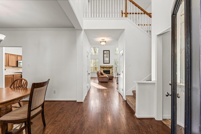 foyer featuring dark wood finished floors, a fireplace, baseboards, a towering ceiling, and stairs