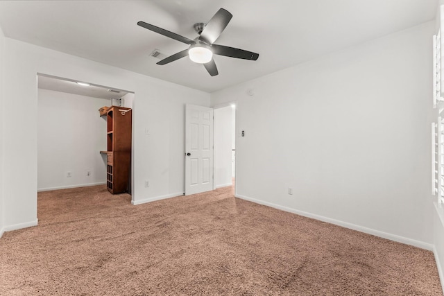 unfurnished bedroom featuring a walk in closet, visible vents, carpet, baseboards, and ceiling fan