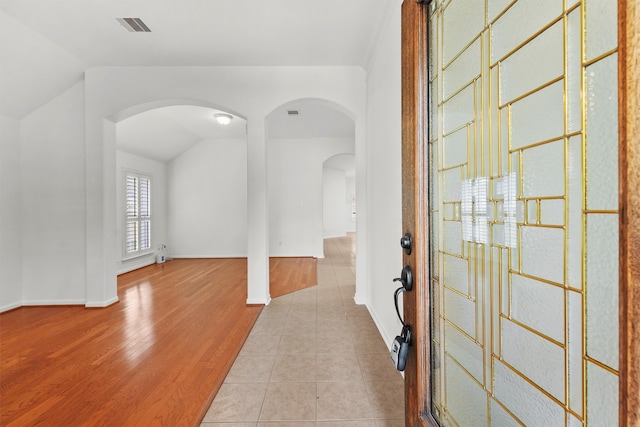 foyer entrance with wood finished floors, baseboards, visible vents, arched walkways, and vaulted ceiling