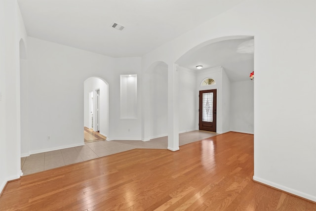 entrance foyer with baseboards, wood finished floors, visible vents, and arched walkways