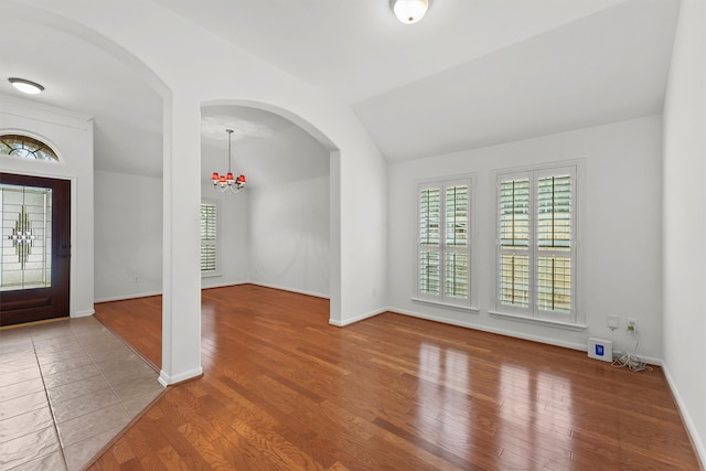 entryway with baseboards, arched walkways, wood finished floors, and vaulted ceiling