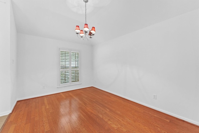 empty room with baseboards, wood-type flooring, and a chandelier