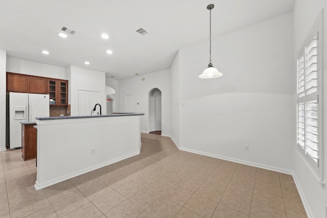 kitchen with visible vents, white refrigerator with ice dispenser, recessed lighting, arched walkways, and glass insert cabinets